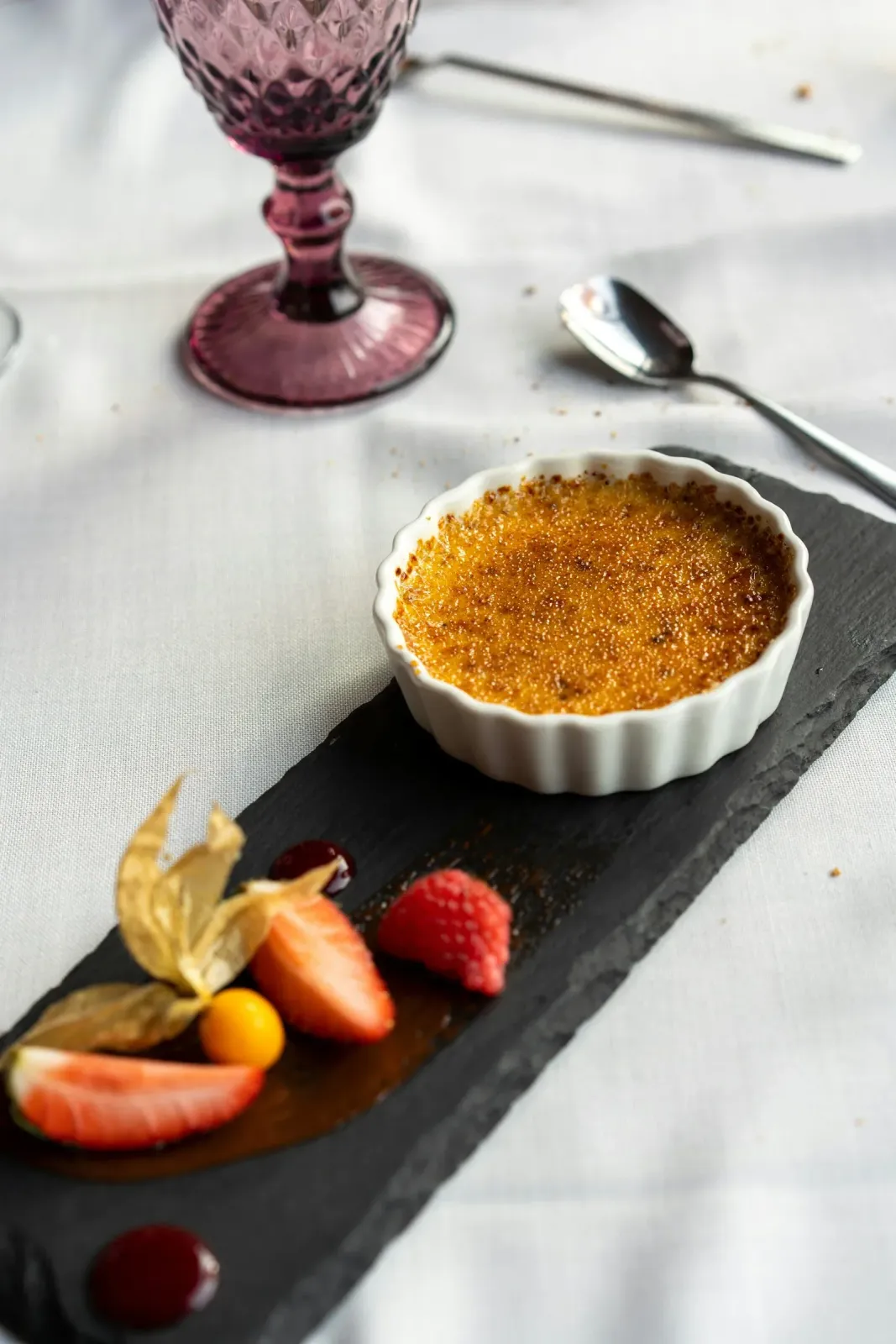 Caramelized custard with berries and a wine glass on a linen-covered table.