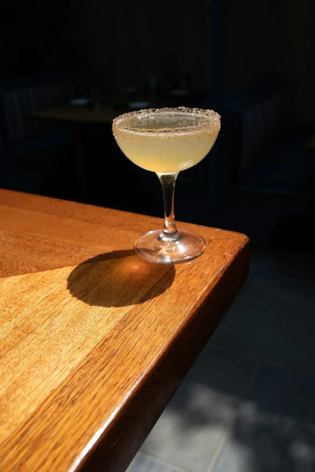 A sunlit cocktail in a stemmed glass on a wooden table.