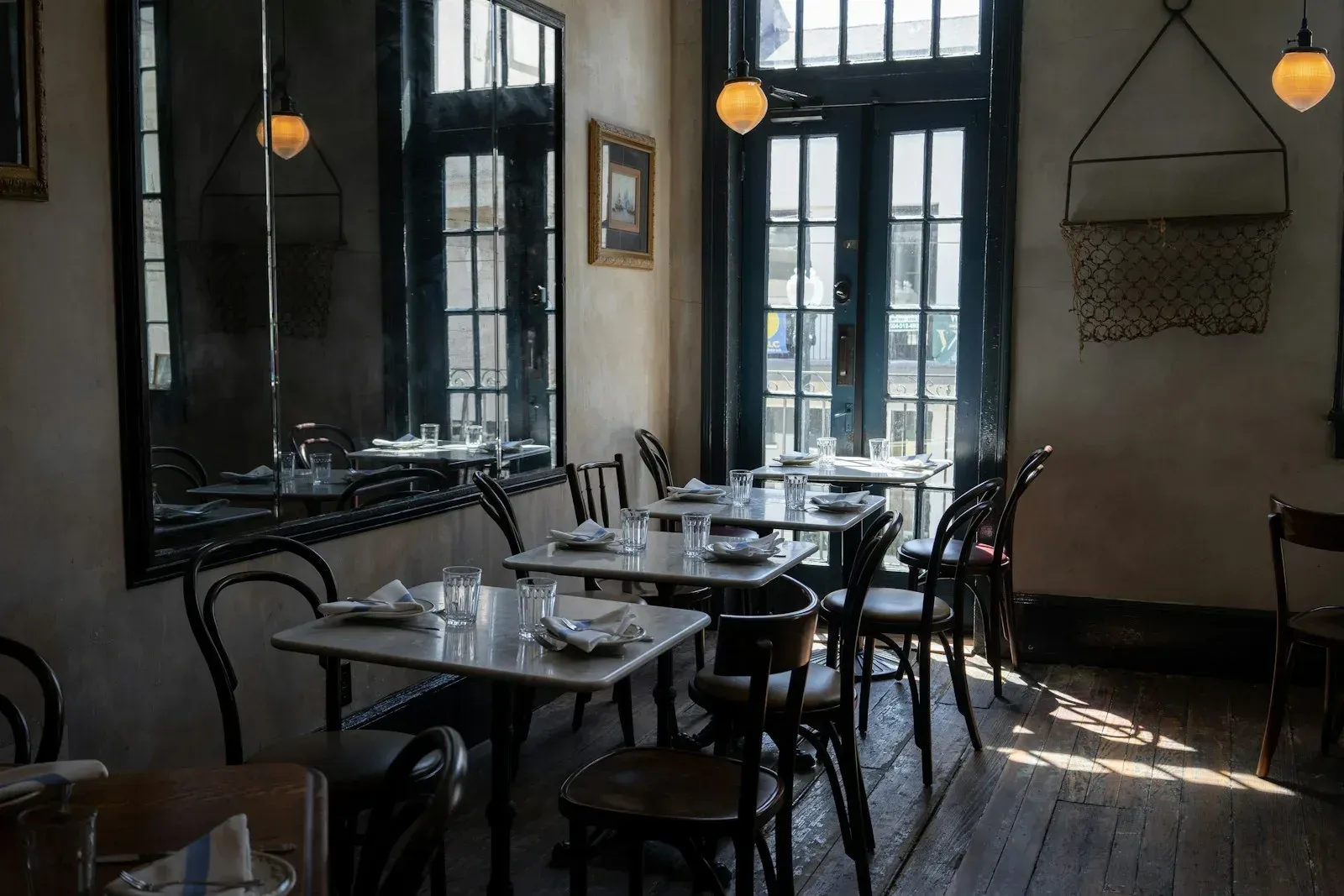 Bistro tables and dark wooden chairs beside tall windows.