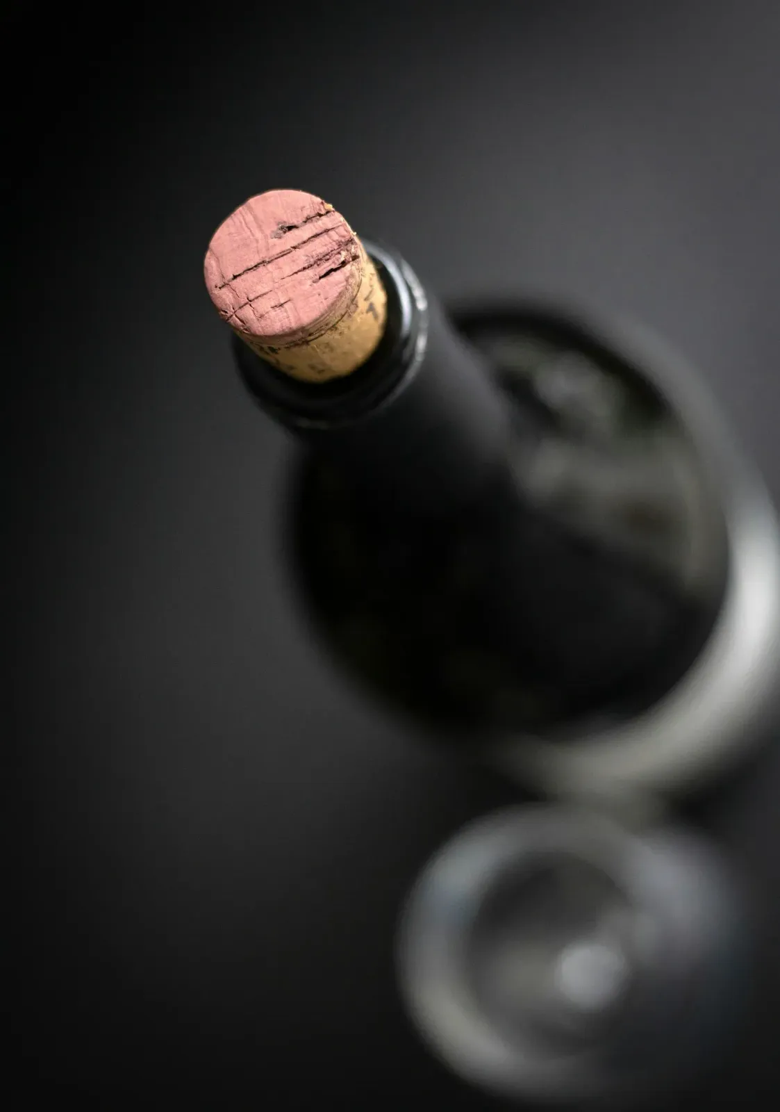 A bottle of red wine and a glass on a dark table.